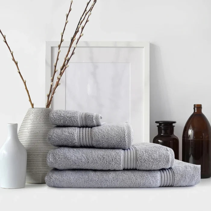 Stacked Colibri Imperial Zerotwist bath sheets in silver, arranged with decorative white vases and pussy willow branches.