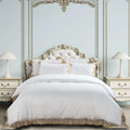 Cotton Co 400-thread-count embroidered queen duvet cover set in white with gold lace trim, shown on an ornate bed.