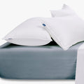 Two white pillows with blue labels resting on a duck egg blue cotton king-size fitted sheet.
