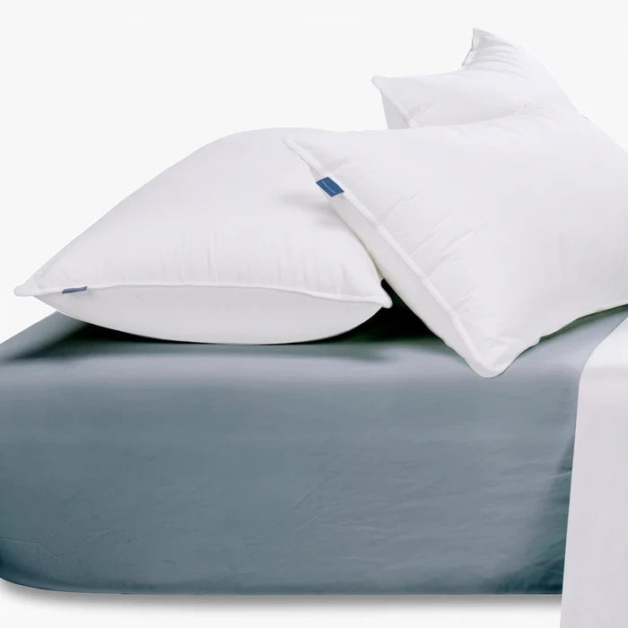 Two white pillows with blue labels resting on a duck egg blue cotton king-size fitted sheet.