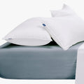 Two fluffy white pillows with blue labels resting on a duck egg blue Cotton Co Queen extra fitted sheet.