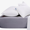 A grey Cotton Co 400 thread count queen fitted sheet with two white pillows resting on it.