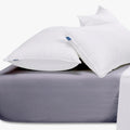 Two white pillows rest on a grey Cotton Co 400 Thread Queen fitted sheet, with a white flat sheet visible at the side.