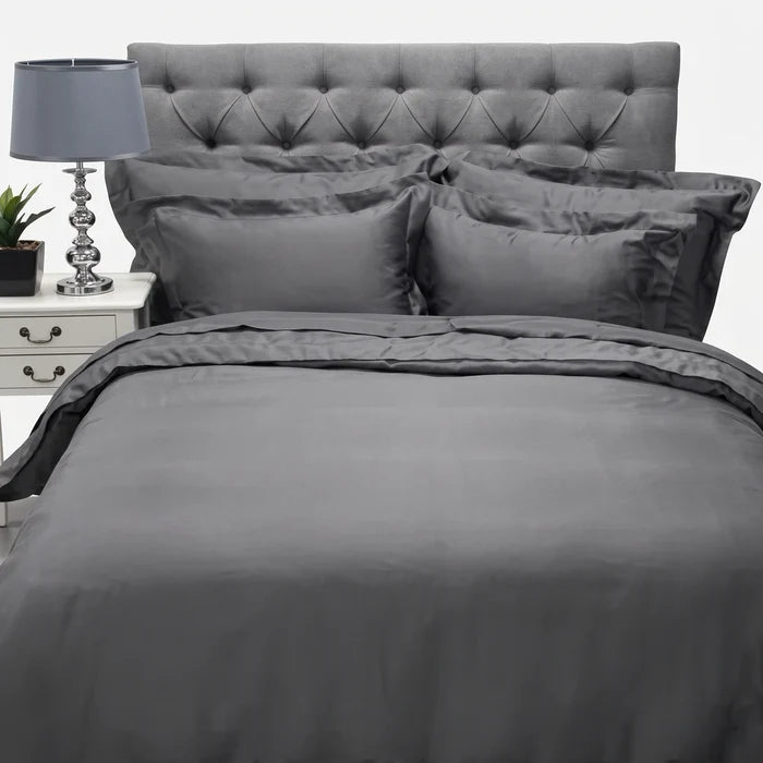 Grey cotton Oxford 400 thread count super king flat sheet displayed on a bed with a tufted headboard, nightstand, and lamp.