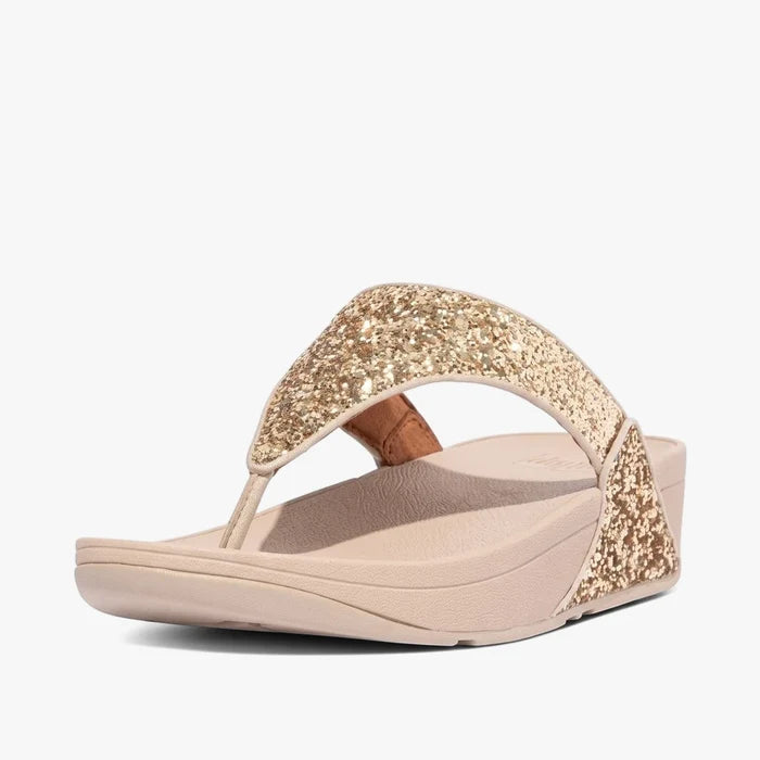 A single Fit Flop Womens Lulu Glitter Wedge Sandal in Platino gold, featuring a sparkly thong strap and a comfortable chunky