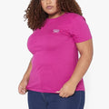 Plus-size woman wearing a vibrant orchid flower pink short-sleeve t-shirt with a small logo, paired with blue jeans.
