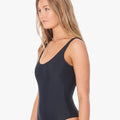 Woman with blonde hair wearing a black Ripcurl Classic Surf Eco One Piece Bikini, captured in a side profile view.
