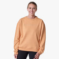 Salomon Womens Heritage Pullover in Apricot Crush, a comfortable crew-neck sweatshirt worn by a woman, providing a relaxed