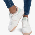Sissy Boy white low-top sneakers with multi pastel accents on a person wearing blue jeans, captured from a low angle.