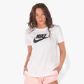 A female model wears a white Nike Essential Icon short sleeve tee with a black logo, paired with light pink shorts, standing